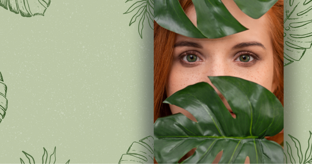 Red-haired woman with green eyes behind tropical leaves – Skin & Glow natural skincare.