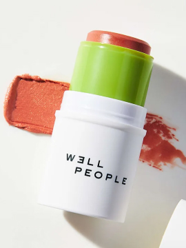 A WELL PEOPLE multi-use stick in a white and green case with a coral-pink blush swatch visible on a clean, white background. Sold by Skin & Glow.